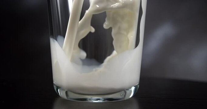 Milk pouring into glass with splash in slow motion close up black background
