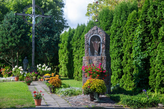 Vilnuis, Lithuania,  Landscaped church garden featuring stone wayside shrine, wooden cross, green hedge, and pathways.  The Roman Catholic Church of St. Bartholomew in Uzupis district,
