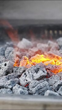 Burning charcoal briquettes glowing with intense orange flames in a backyard barbecue grill