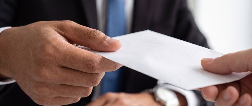 A business person handing a white envelope to another person in a formal setting