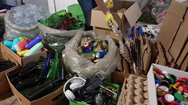 Hands sorting recyclable materials into labeled recycling bins for plastic, paper, glass, metal, and electronics. Waste separation and circular economy concept
