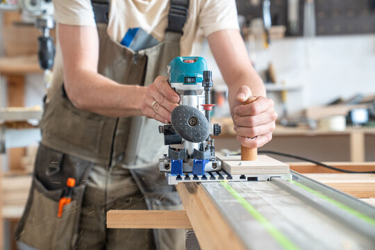 Carpenter technician using handheld wood router machine with track for vintage wooden door restoration, man holding tool connected by adapter to metallic guide rail with custom-built wooden handle.