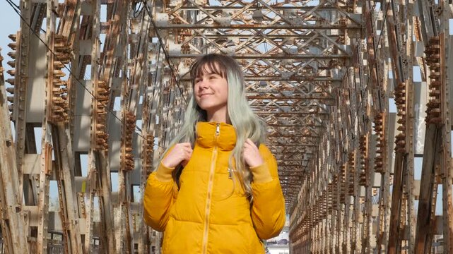 Active teen on rusty bridge. A stylish girl with backpack have a traveling promenade on the old urban bridge in the day light