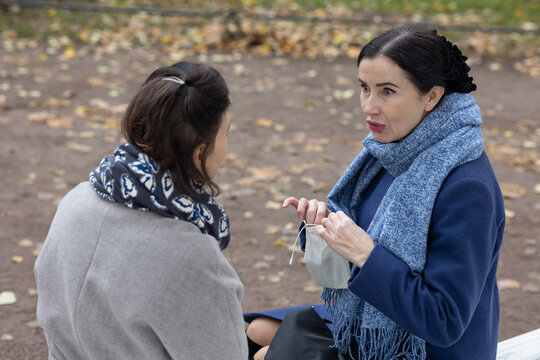 Communication. Two female friends meeting outdoors in city park sharing emotional talk and gestures during cool seasonal daytime.