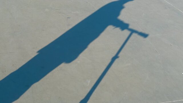 Shadow of person riding electric scooter. Elongated silhouette casting stark shadow while riding electric scooter across gray concrete urban surface under bright sunlight