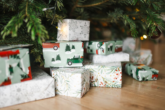 Wrapped Christmas gifts arranged under a decorated evergreen tree at home. Festive presents, warm lights and natural fir branches create a cozy holiday atmosphere.