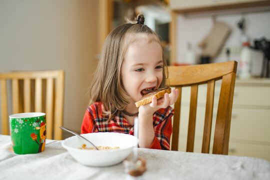 Young child eating toast with chocolate spread at the breakfast table in a cozy home kitchen. Festive details create a warm Christmas holiday morning atmosphere.
