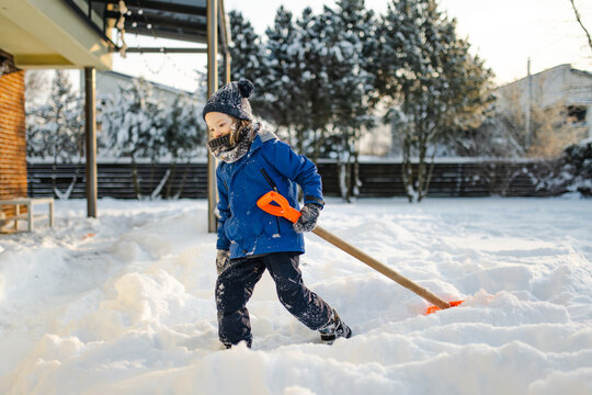Young child helping shovel deep snow in a backyard on a sunny winter day. Playful outdoor household chore teaches responsibility and participation in family life.