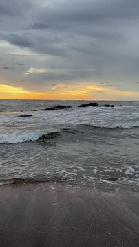 Waves roll onto the shore as the sun sets over the ocean creating orange and gray skies in the evening.
