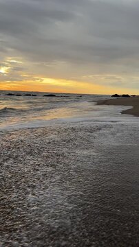 Footprints appear on the sand as the sun sets over the ocean. Waves gently wash ashore.