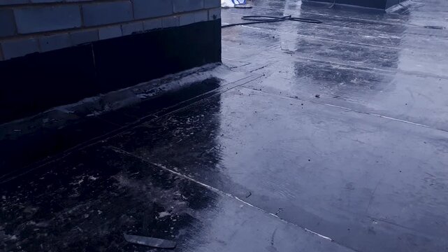 Roofing felt. A building roof covered with roofing felt with a bitumen base. Roof waterproofing; bitumen based moisture insulation for roofs. Industrial work with roofing felt.