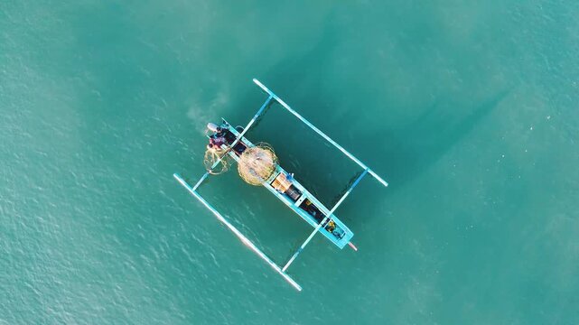 Top down aerial drone view of traditional Balinese jukung outrigger fishing boat with fisherman preparing net on turquoise sea water. Yeh Gangga Bali Indonesia. Minimalist ocean aerial