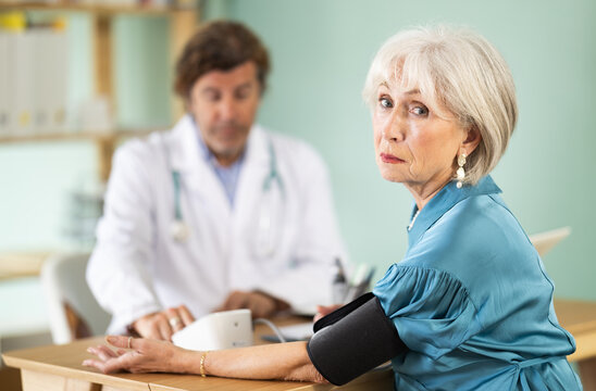 Sad mature female patient undergoes blood pressure measurement procedure in doctors office. Diagnosis of state of health to determine causes of disease, annual medical examination.