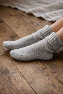 Close-up of cozy woolen knit socks on feet resting on a wooden floor at home.