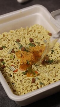Vertical video. Chef pours hot boiling water from kettle, over quick cooking instant egg curly noodles, ramen with spices, herbs in plastic packaging for soup and Asian plates. Healthy fast food