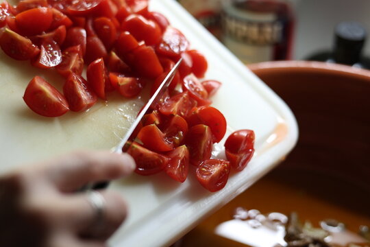 Tomates cerises coup&eacute;es transf&eacute;r&eacute;es d'une planche dans un plat en terre cuite