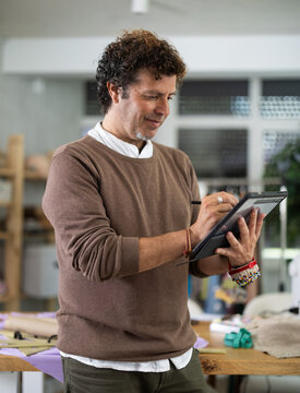 Adult man dressmaker draws pattern on tablet in sewing workshop