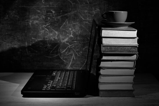 Stack of books and a laptop computer. Back to school, education, learning,home office, knowledge concept.Monochrome shot.