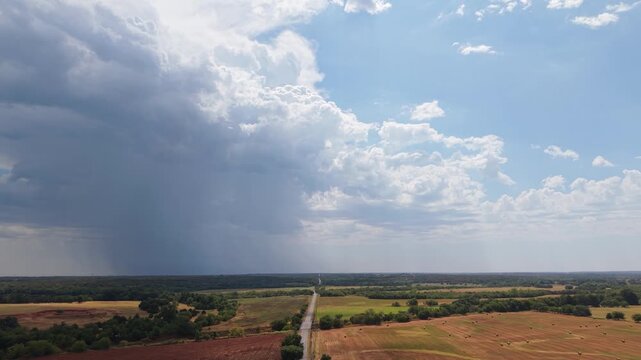 Aerial view of a rural road through farmland under split weather with dark storm clouds and sunny sky, Oklahoma