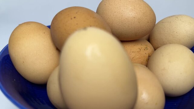Brown and cream organic eggs stacked inside a glossy blue bowl with soft lighting and smooth textures. Perfect for healthy cooking or breakfast blog posts.