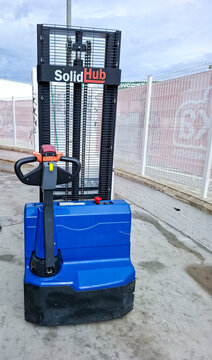 Denia, Spain - October 10, 2025. Blue SolidHub electric pedestrian stacker forklift parked near a chain link fence in Spain during the day