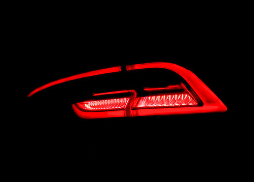 Modern car rear tail light glowing in the dark close up. This is an automotive red LED lighting system line. Bright diode taillight lamp element shining on a black background. Contemporary transport  