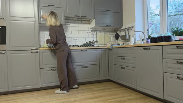  Female carefully wipes upper cabinet doors removing dust and stains.