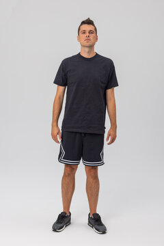 Full-body portrait of a young athletic man in a black t-shirt, shorts, and sneakers standing against a white studio background. Ideal for streetwear, apparel design, or sportswear mockups.