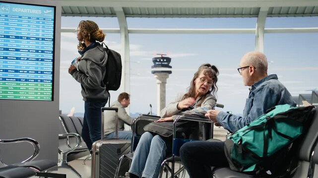 Woman with a disability travels with an older man through an airport lounge as he assists with flight details, reflecting accessibility and equality.