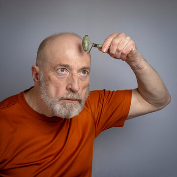senior man is using a jade stone roller for a face massage, skin care routine concept