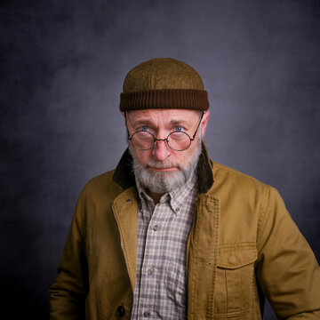 portrait of a seriouis, bearded senior man wearing a docker cap and looking over glasses