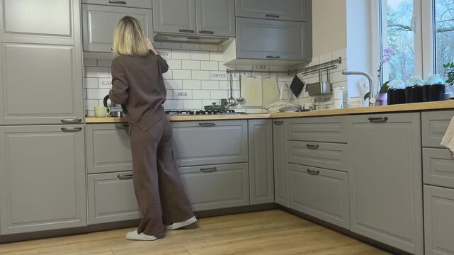 Female wipes upper cabinets keeping kitchen tidy and clean.