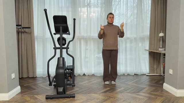 Woman in warm indoor outfit slowly rotates head right and left stretching neck muscles. Gentle mobility routine in living room.