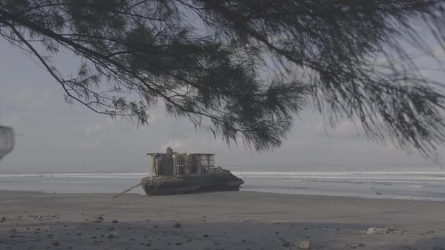 Balinese Hindu sea temple shrine on rock formation at black sand Yeh Gangga Beach Bali. Pine tree branches foreground framing sacred pura with ocean waves. Apple Log flat profile for color grading