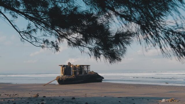 Cinematic view of Balinese Hindu sea temple pura on rock at Yeh Gangga black sand beach Bali. Framed by pine tree branches with ocean waves in background. Tropical spiritual cultural landmark
