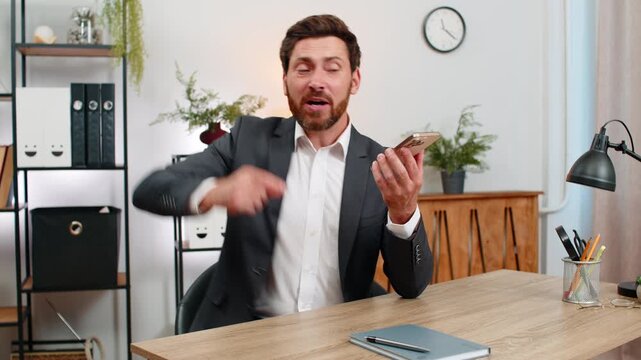 Middle-aged businessman at home office argues on smartphone speaker shouting very waving hand during call. Freelancer guy at table ends conversation sighs angrily staring at device feeling frustrated.