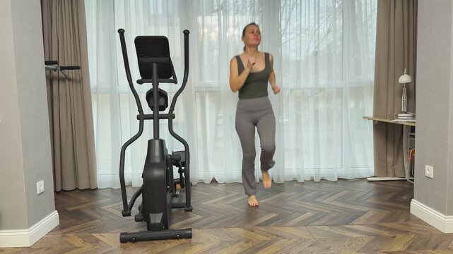 Woman runs in place with small jumps and bent arms in rhythmic motion. Home interval cardio improving endurance, coordination and fitness level.