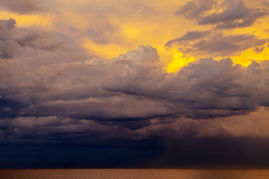 Mare calmo con temporale all'orizzonte con nuvole colorate dal tramonto