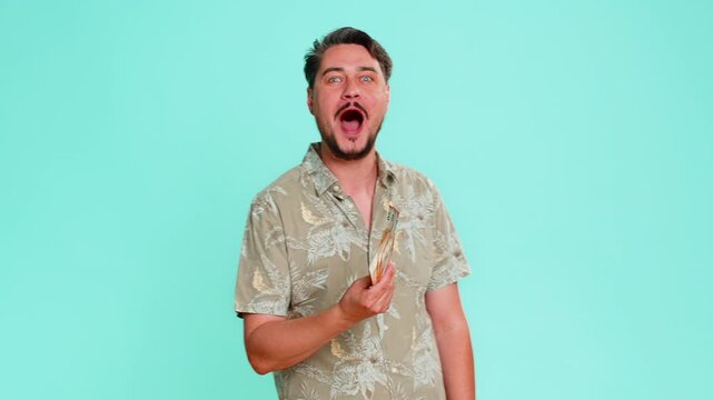 Middle-aged man joyfully holds a pile of euro cash money, raises hands in triumph smiles celebrating big win received prize salary bonus. Young adult guy isolated on blue background expressing success
