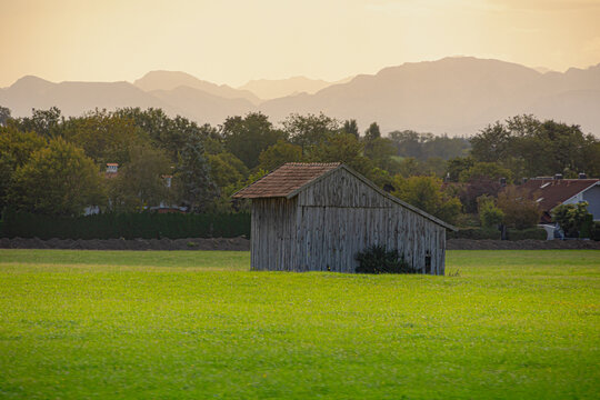 Bavarian countryside landscape, A traditional wooden barns standing alone on a rolling hill, Lush green grass meadow against majestic Alpine mountains under blue sky and white clouds, Bavaria, Germany