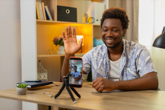 African American young man on home table records story on smartphone and shares important news with followers. Black guy on home table talks to camera and shares important information with followers.
