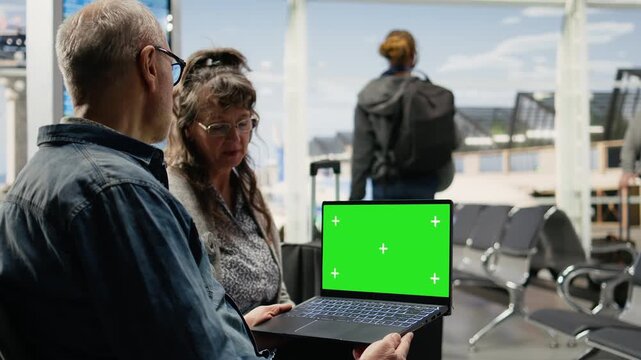 Chroma key laptop screen is used by senior travelers in an airport lounge as they check an itinerary and plan their next retirement adventure.