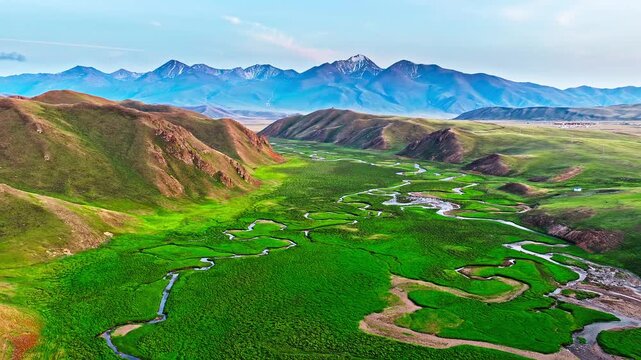 Aerial drone view of a river winding through lush green wetland meadow in Bayinbuluke Grassland, Xinjiang, China