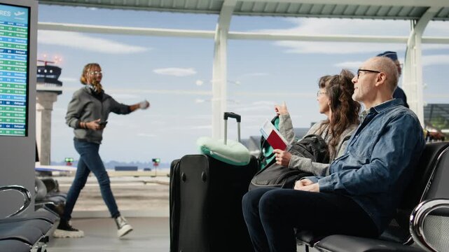 Cheerful pensioners wait in an airport seating area with a suitcase chatting and enjoying time together while reflecting a carefree active retirement lifestyle.