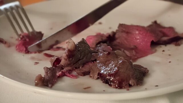 Person slicing juicy picanha roast beef with fork and knife on white plate, close-up of Brazilian churrascaria-style grilled steak being enjoyed at restaurant table. Elegant luxury romantic dinner