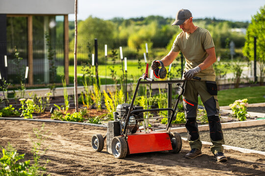 Gardener holding earmuffs beside a lawn scarifier