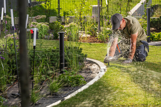 Gardener working on a sprinkler beside a lawn border