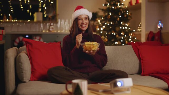Woman in Santa hat eating chips while watching movie at home, 4K