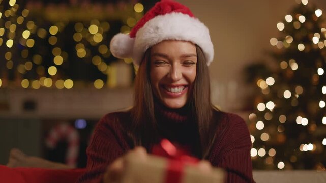 Woman in Santa hat reacting joyfully to Christmas present at home, 4K