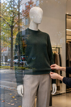 Retail worker adjusting autumn clothing on a store mannequin with seasonal foliage reflected in the fashion shop window